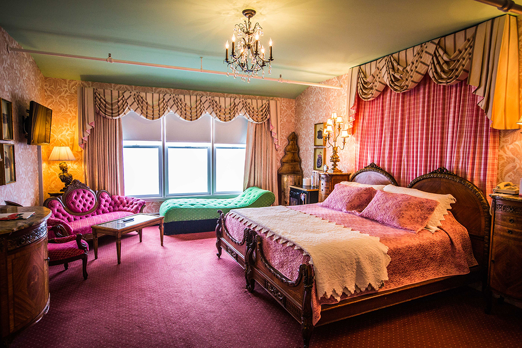 Image of the Signature Suite with pink silk covers displayed on king-size bed and velvet couch. Grand Hotel, a member of Historic Hotels since 2001, dates to 1886. It is located in Mackinac Island, Michigan.